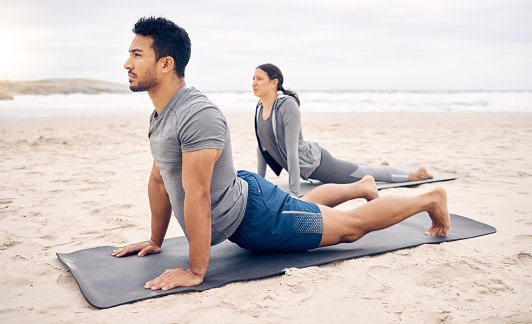 Exercise, yoga and wellness with a couple on the beach for a mental health or awareness workout in the morning. Fitness, pilates or mindfulness with a young man and woman by the ocean or sea for zen