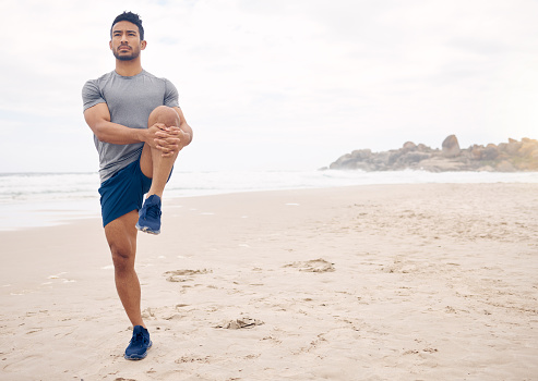 Fitness, stretching and space with a man on the beach at the start of his workout for health or wellness. Exercise, thinking and warm up with a young athlete training outdoor by the ocean or sea