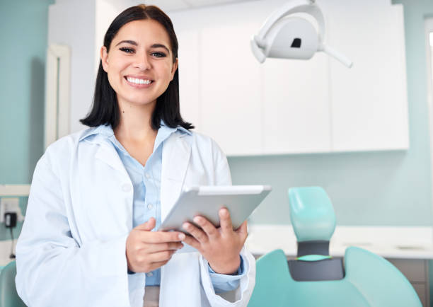 Happy, tablet and portrait of woman dentist with confidence in her office doing research at clinic. Smile, medical and young female orthodontist or dental doctor with digital technology in hospital. stock photo