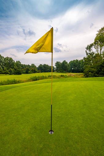 Golf course with yellow flag on 18th hole against a cloudy sky