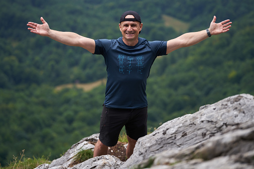 Strong athletic man on top of the mountains with forest in distant background
