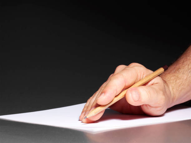An old wrinkled hand holding a pen against a white paper background