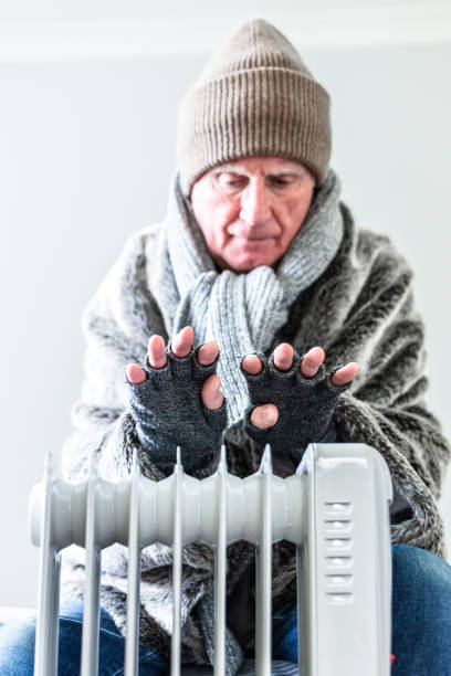 istock Cold senior man warming his hands over electric heater at home 1816805162