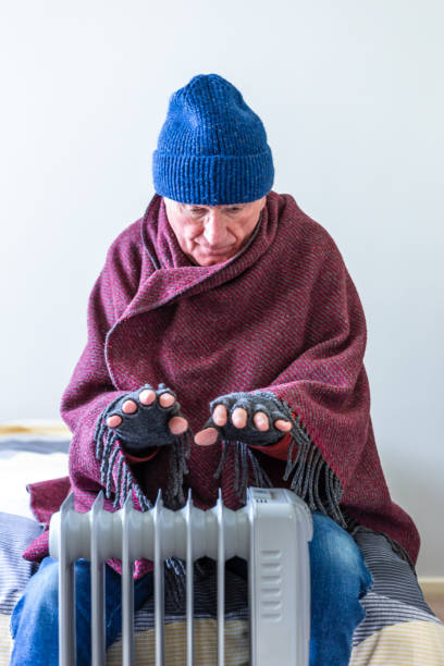 istock Cold senior man warming his hands over electric heater at home 1816805711