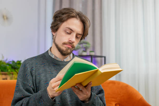 istock Bearded man reading interesting book turning pages smiling enjoying literature taking a rest at home 1816814616