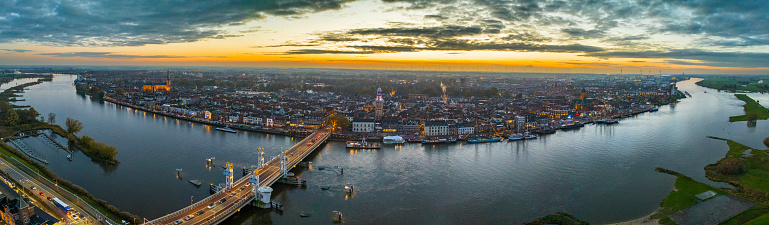 Kampen on the banks of the river IJssel during sunset seen from above with the Koornmarktspoort and Bovenkerk in the old town of Kampen during an autumn sunset. The koornmarktspoort is the oldest gate of Kampen located at the riverbank of the IJssel. The Bovenkerk or the Church of St. Nicholas is a large, Gothic church and the most striking element on the skyline of Kampen at the river IJssel in the Overijssel province.