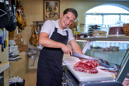 A portrait of an spanish butcher looking at the camera cutting meat in a Spanish butcher shop