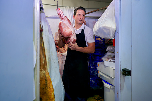 A Spanish butcher from a neighborhood butcher shop takes a piece of meat out of the refrigerated chamber to cut