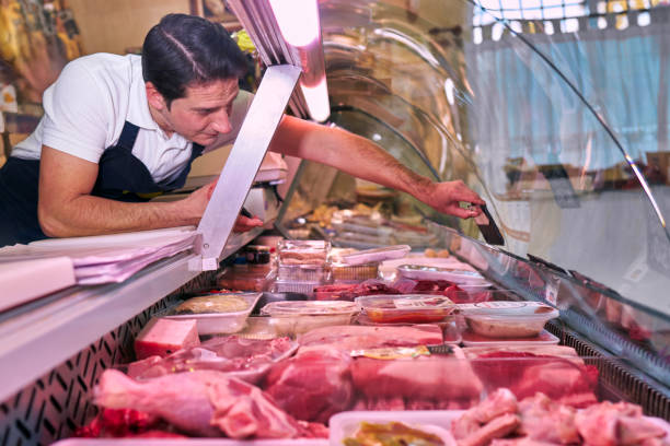 A Spanish butcher from a neighborhood butcher shop places the price of a meat inside the refrigerator display You can see the meat display with all kinds of meat and the butcher selecting the sirloin weisswurst photos stock pictures, royalty-free photos & images
