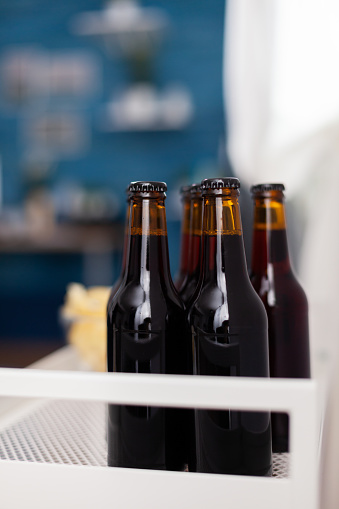Close up of dark beer bottle in elegant apartment. Modern living room with nobody in with blue furniture and walls, beautiful decorated. Pretty simple decor of apartment. Elegant retro decoration, cozy.