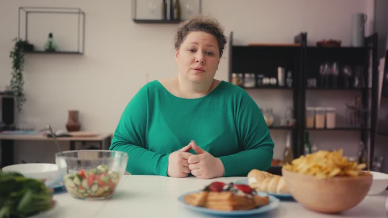 Overweight woman choosing between healthy food and unhealthy snacks, dieting