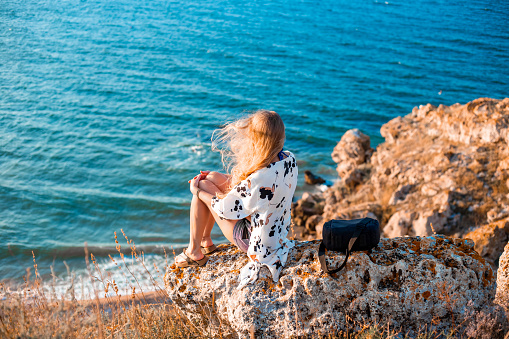 A woman with flowing hair sits on a mountain top and looks out to the sea. Travel and tourism.