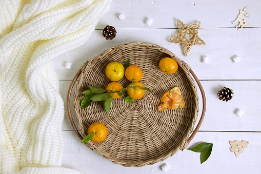 Round wicker tray with tangerines on wooden table. Cozy winter composition, festive Christmas background. Top view, flat lay.