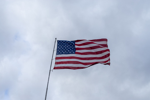 White flag attached to a flagpole waving on the sky