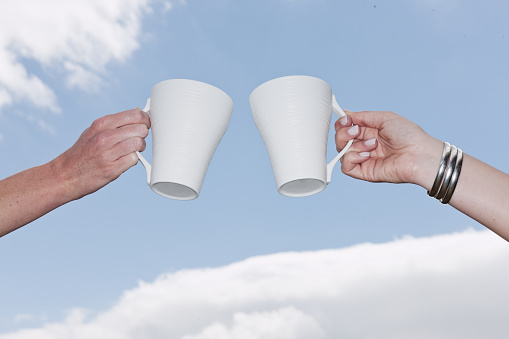 Here's to friendship! Two young woman holding their coffee cups aloft.