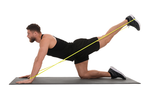 Young man exercising with elastic resistance band on fitness mat against white background