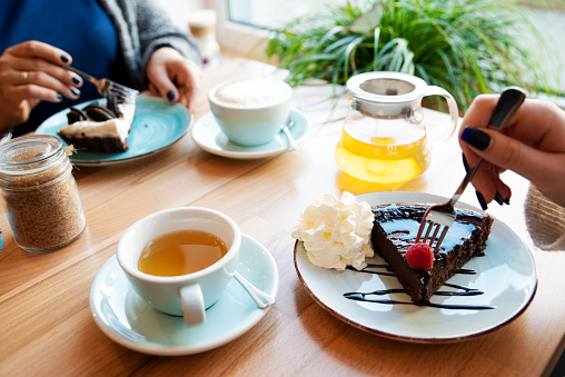 Slice of chocolate cake on a plate with fork in hand of woman in cafe. Sweet Food and drink. Table and Close-up.