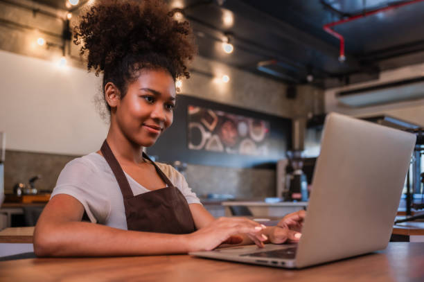 istock Cute young black female waitress barista using a laptop computer to check orders with happiness in the cafe at restaurant. 1816965042
