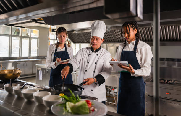 istock Professional senior male chef teaching his multiracial ethnic diversity female students in kitchen at restaurant. 1816970899