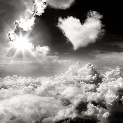 A black and white picture of gorgeous clouds and a heart shaped cloud flooding in the sky while sun is shining through,\nangelic sky in b&w with a heart shaped cloud