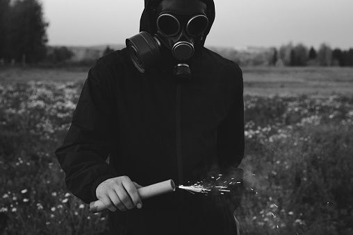 Man in black clothes wearing a gas mask and black smoke bomb in a field. The concept of ecological catastrophe or nuclear war.