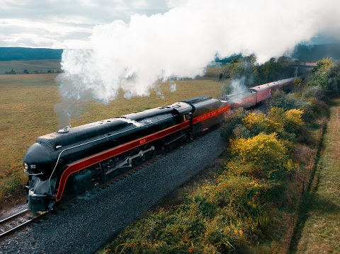 Staunton, United States – October 07, 2023: A close-up view of a black and red train parked on a set of railroad tracks, surrounded by lush green foliage