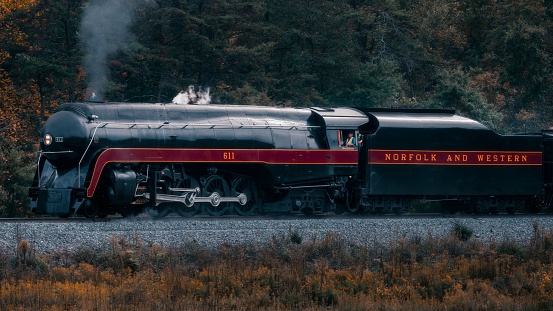 Staunton, United States – October 06, 2023: An old-fashioned steam train chugging through a lush, green forest, surrounded by tall trees