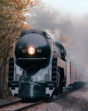 Staunton, United States – October 07, 2023: A high-angle view of a majestic steam-powered locomotive moving down a set of train tracks, surrounded by a thick fog that has settled in a lush