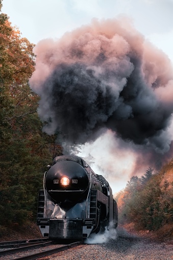 Staunton, United States – October 07, 2023: A vintage steam locomotive emitting a billowing cloud of grey smoke as it chugs along the tracks