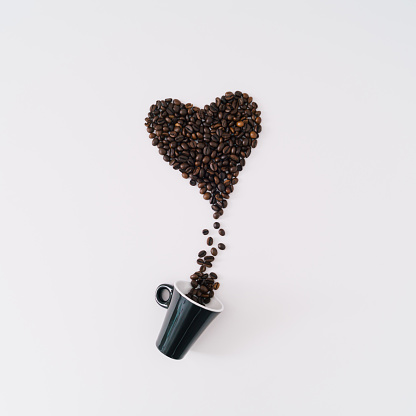 Creative composition with heart shape made of roasted coffee beans and coffee cup on white background. Realistic aesthetic look. Contemporary style. Minimal love concept. Unique flat lay.