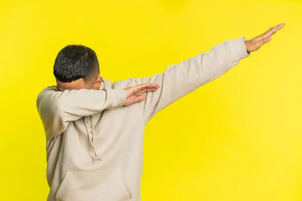 Photo of Happy Indian man having fun dancing moving to rhythm dabbing raising hands, making dub dance gesture