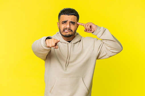You are crazy, out of mind. Confused Indian man pointing at camera and showing stupid gesture, blaming asking some idiot for insane plan, bullying. Arabian guy isolated on yellow studio background