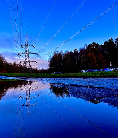 An electricity pylon and cables reflected in stagnant water against dramatic cloudscape
