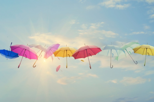 Conceptual photo of different color umbrellas lined-up across the sky. Sun is behind them shining, and this concept can represent team work, individuality, success of different people working together etc.