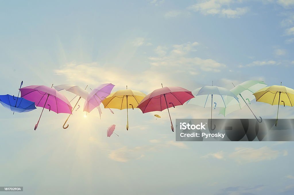 Umbrellas line-up across the sky Conceptual photo of different color umbrellas lined-up across the sky. Sun is behind them shining, and this concept can represent team work, individuality, success of different people working together etc. Umbrella Stock Photo