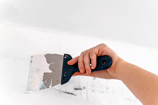 A woman's hand with a spatula applies putty to the wall