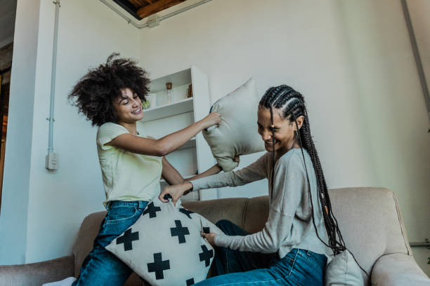 Young sisters playing pillow fight on sofa in the living room at home