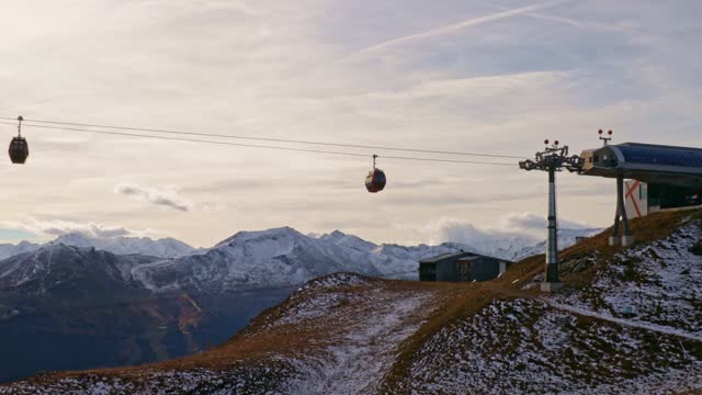 Cable car cabins move between stations against the background of red slopes, snow-capped mountains and cloudy skies, Austrian Alps