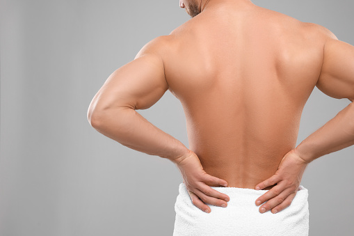 Man suffering from back pain on grey background, closeup. Space for text