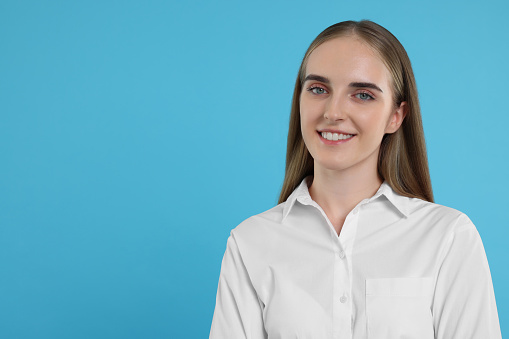 Portrait of happy young secretary on light blue background, space for text