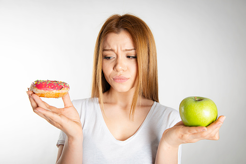 Woman's hands holding donut and apple.