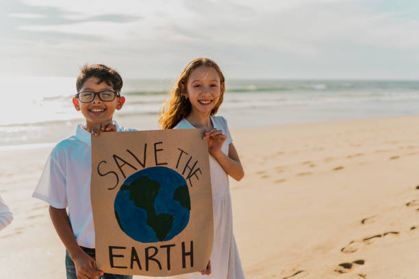 портрет детей, держащих плакат протеста за спасение планеты земля на пляже - community outreach child social worker waist up стоковые фото и изображения