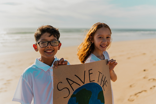 Portrait of children holding a sign protesting to save planet Earth on the beach