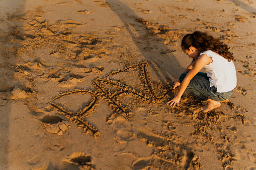 Child girl writing Peace (in Spanish and Portuguese language) in the sand on the beach