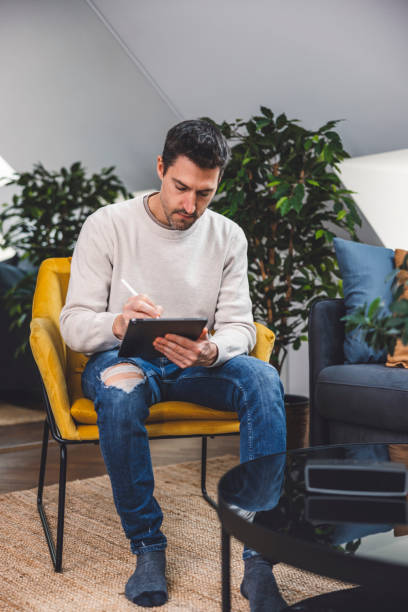 istock Man using smart devices in his living room. Smart speaker dancing, thermostat, tablet, robot vacuum cleaner, checking security cameras. 1817147013