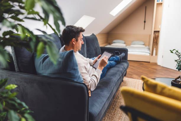 istock Man using smart devices in his living room. Smart speaker dancing, thermostat, tablet, robot vacuum cleaner, checking security cameras. 1817147478