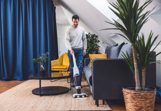 istock Man using smart devices in his living room. Smart speaker dancing, thermostat, tablet, robot vacuum cleaner, checking security cameras. 1817150539