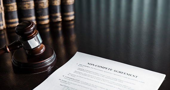 Close up of a non-compete clause agreement with a gavel and books.