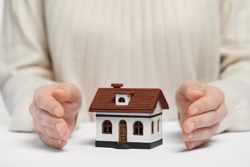 Home security concept. Woman with house model at white table, closeup