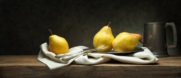 istock Three pears on old wooden table in vintage setting with cutlery, plate and pewter mug, space for text. 1817217047